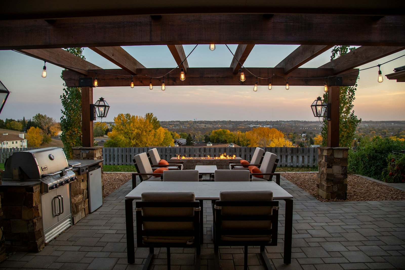 Built-in outdoor kitchen with a grill beneath a timber pergola