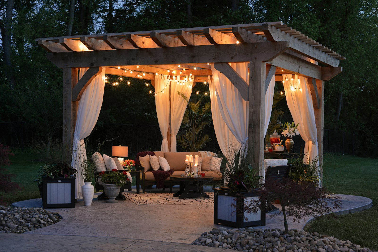Pergola lit at night with drapes and string lights